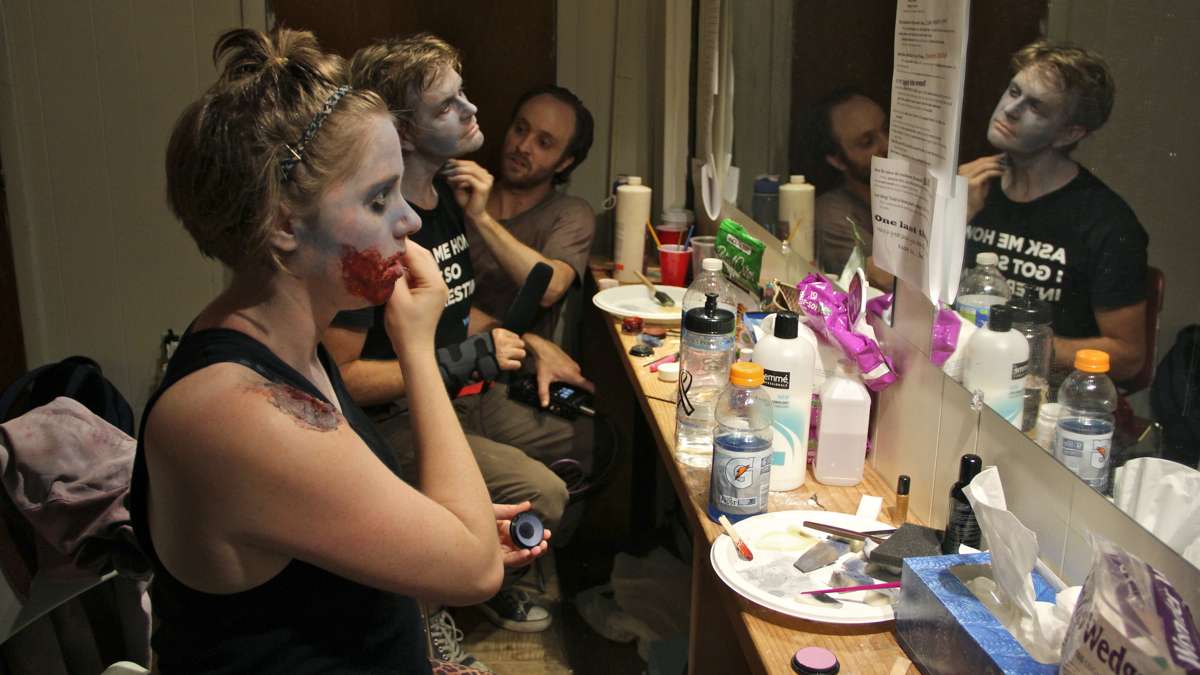 Tara Demmy touches up her makeup while Peter Crimmins gets some help from Kyle Yackoski in the dressing room at the Luna Theater. (Emma Lee/WHYY)