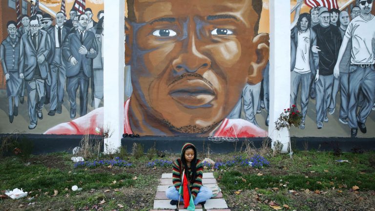  In a Dec. 16, 2015 file photo, Jazmin Holloway sits below a mural depicting Freddie Gray at the intersection of his arrest, in Baltimore. (Patrick Semansky/AP Photo, File) 