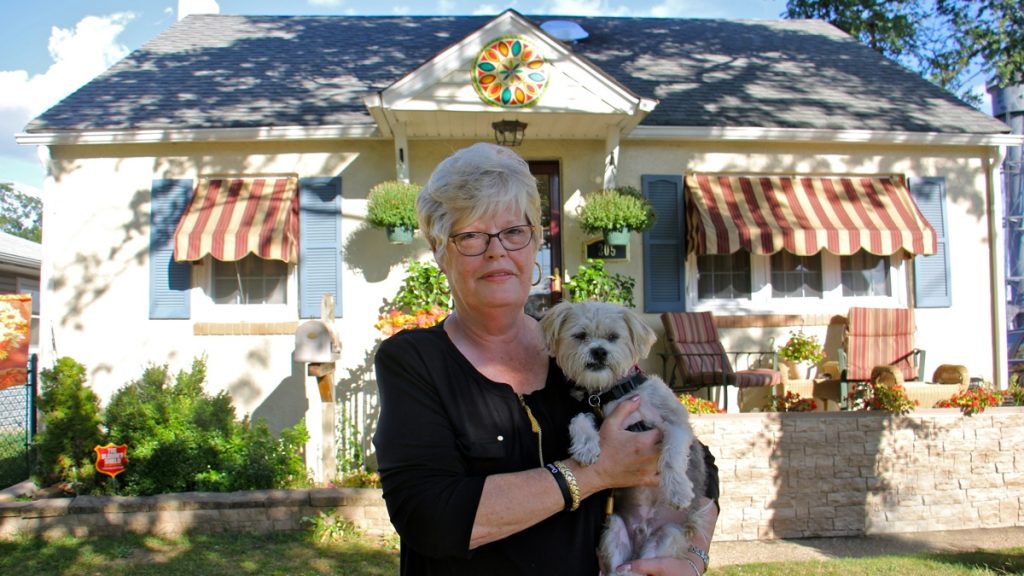 l_2017-09-20-e-lee-betty-paulson-paulsboro-home-ownership-declines-while-rentals-increase A woman with white hair stands in front of her yellow house, holding her white haired dog