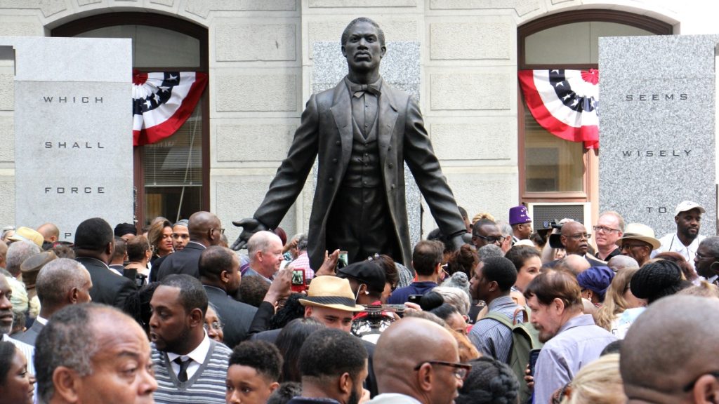 l_2017-09-26-e-lee-philadelphia-city-hall-octavius-catto-monument-statue A statue of Octavius Catto at it's unveilling - statue facing front with arms spread open and back, people in the foreground in Philadelphia