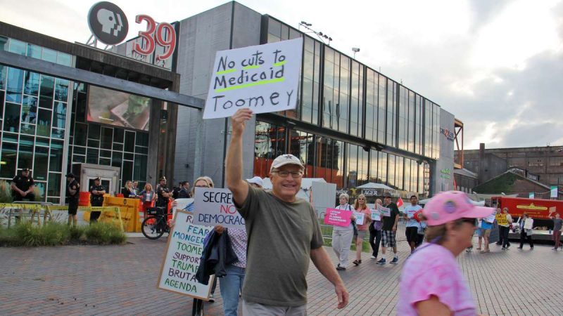 Protesters parade outside the PPL Public Media Center in Bethlehem where U.S. Sen. Pat Toomey held a town hall meeting televised by PBS 39. (Emma Lee/WHYY)