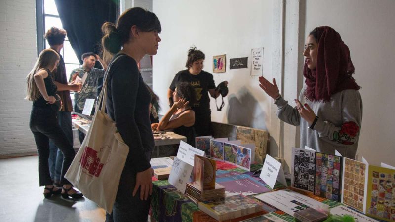 Bushra Alfaraj (right) chats with a YallaPunk attendee about different MENA programing around Philadelphia. (Emily Cohen for WHYY)