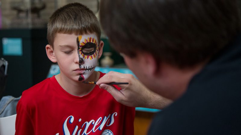 A man paints half of a boy's face to look like a skull