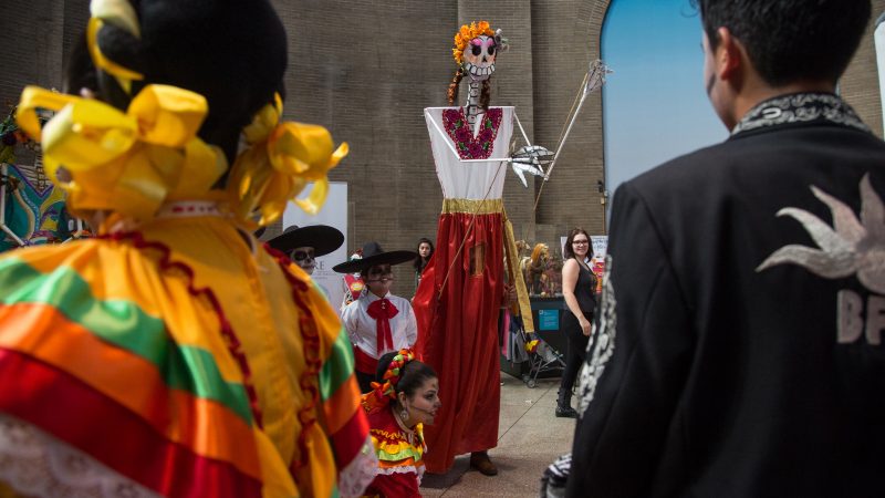 A large skeleton puppet dances with traditional Mexican dancers at a day of the dead celebration