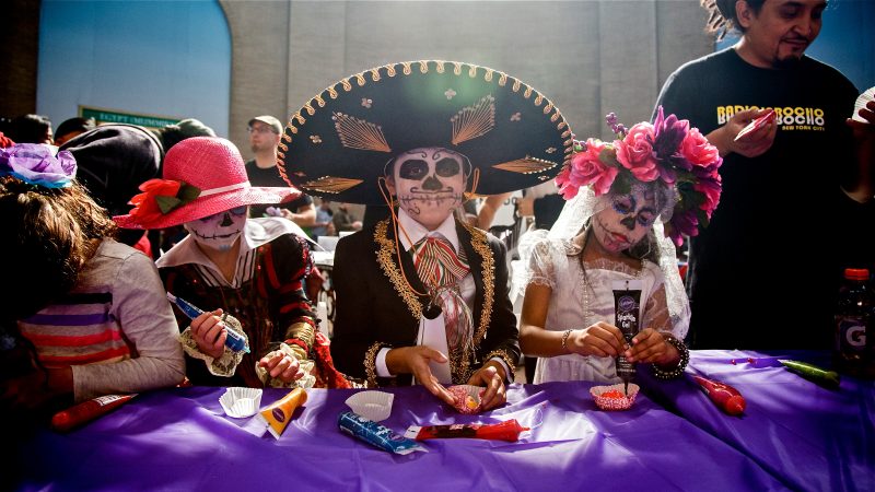 Costumed children in skull face paint decorate sugar skulls