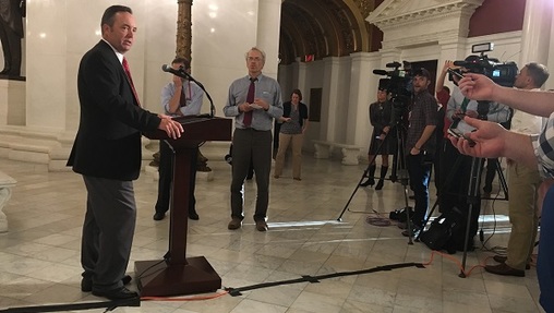 A man stands at a podium, addressing the press