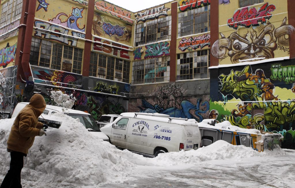 Winter Weather NYC A warehouse covered in large grafiti art; In the foreground, a man shovels snow.