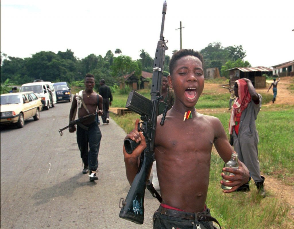 DRUNK AND HAPPY A child soldier; intoxicated and shirtless, holds a rifle