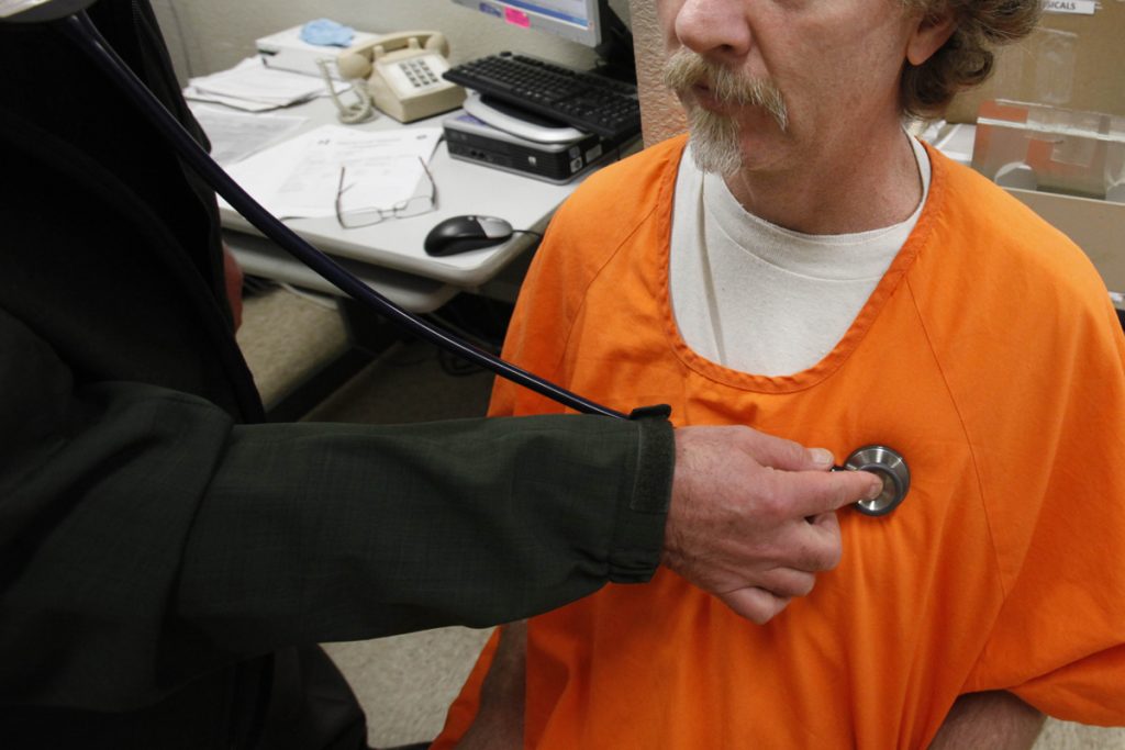 California Prisons A person holds a stethoscope to the chest of a man in an orange prison jumpsuit