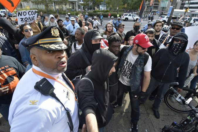 An officer looks to the distance, behind him a group of protesters