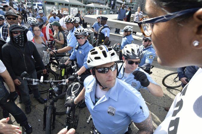 An officer looks to the distance, behind him a group of protesters