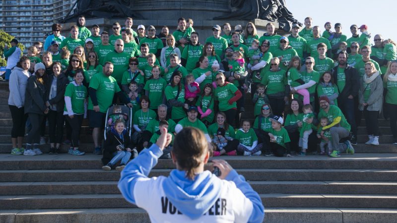 Members of a team, all in green, post on the steps of the Art Museum for a photo before the walk