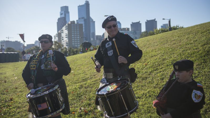 Bagpipers on a grassy knole, city skyline in the background
