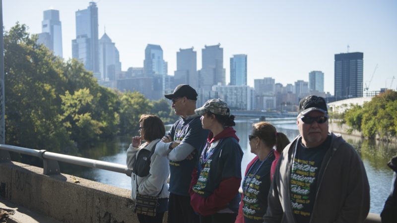 People in matching t-shirts stand against a railing with the city's skyline in the background