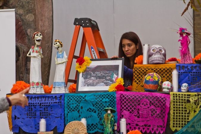 Ivette Compton, with Philadelphia’s Mexican Consulate, adjusts a photo of destruction from earthquakes in Mexico City. (Kimberly Paynter/WHYY)