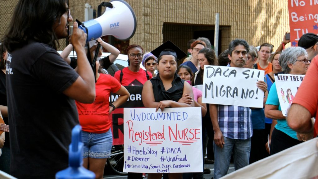l_2017-09-05-e-lee-anel-medina-philadelphia-daca-registered-nurse-undocumented-dreamer A woman speaks through a bullhorn, immigrants hold signs, listen to her speak during a rally