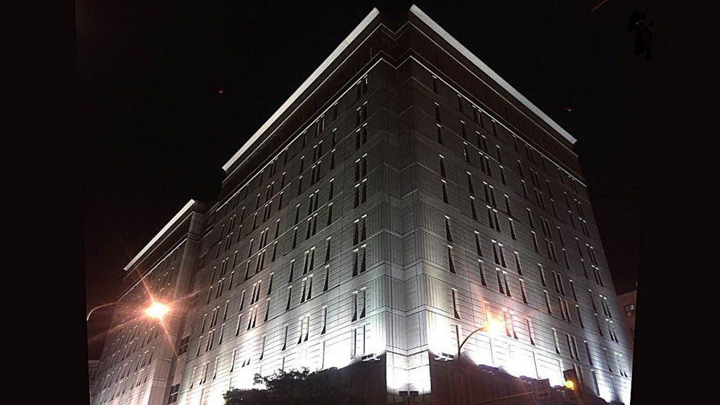 l_20171005-fed-detential-center Bright lights illuminate an imposing grey stone building against a dark night sky