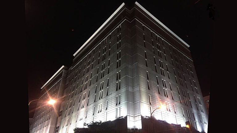 Bright lights illuminate an imposing grey stone building against a dark night sky