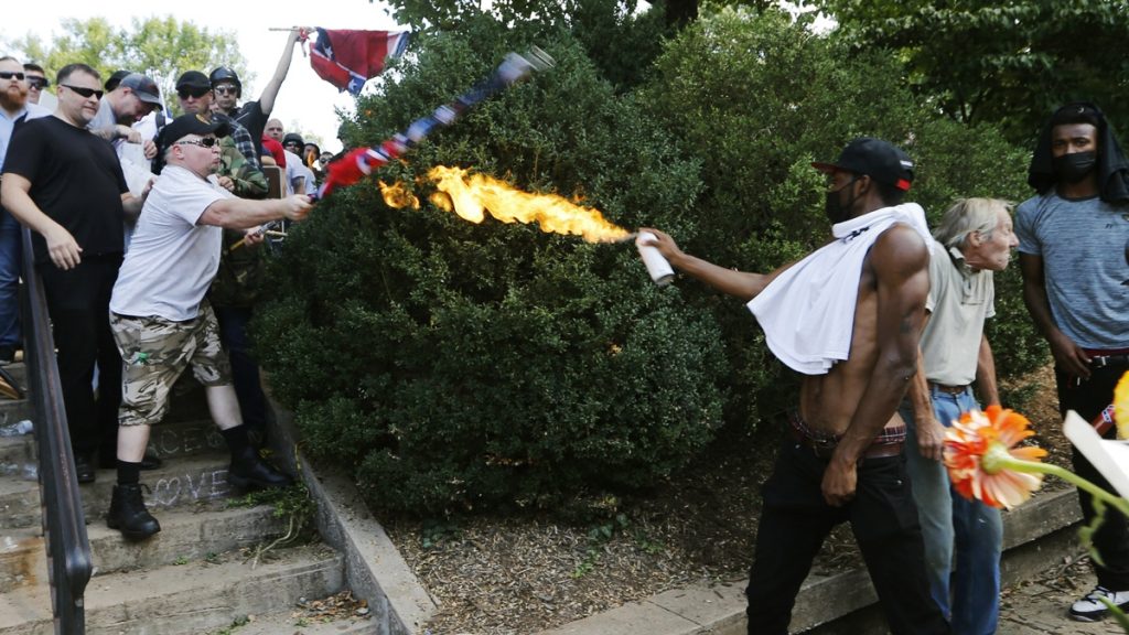 A counter demonstrator uses a lighted spray can agains an Alt Right demonstrator at the entrance to Lee Park in Charlottesville, Va., Saturday, Aug. 12, 2017.