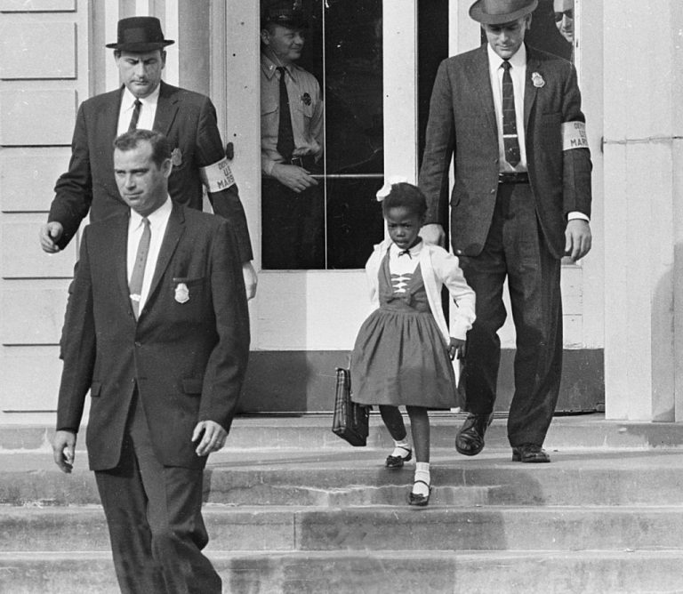 little girl in bobby sock walks down stair surrounding by suited men