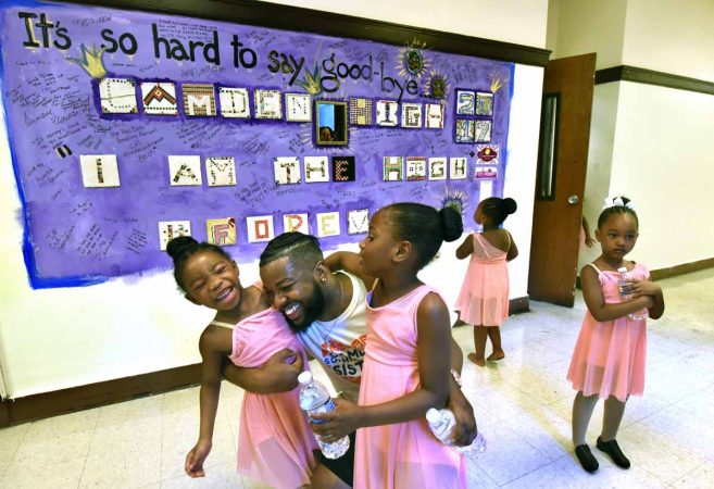 During a June performance at Camden High, members of the Camden Sophisticated Sisters embrace in front of a bulletin board that students used to say goodbye to the school. (April Saul/for Newsworks)