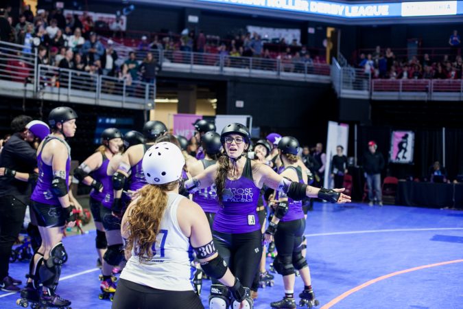 Members of the Rose City Rollers and the new international champions, the Victorian Roller Derby League, hug after the championship game. (Brad Larrison for WHYY)