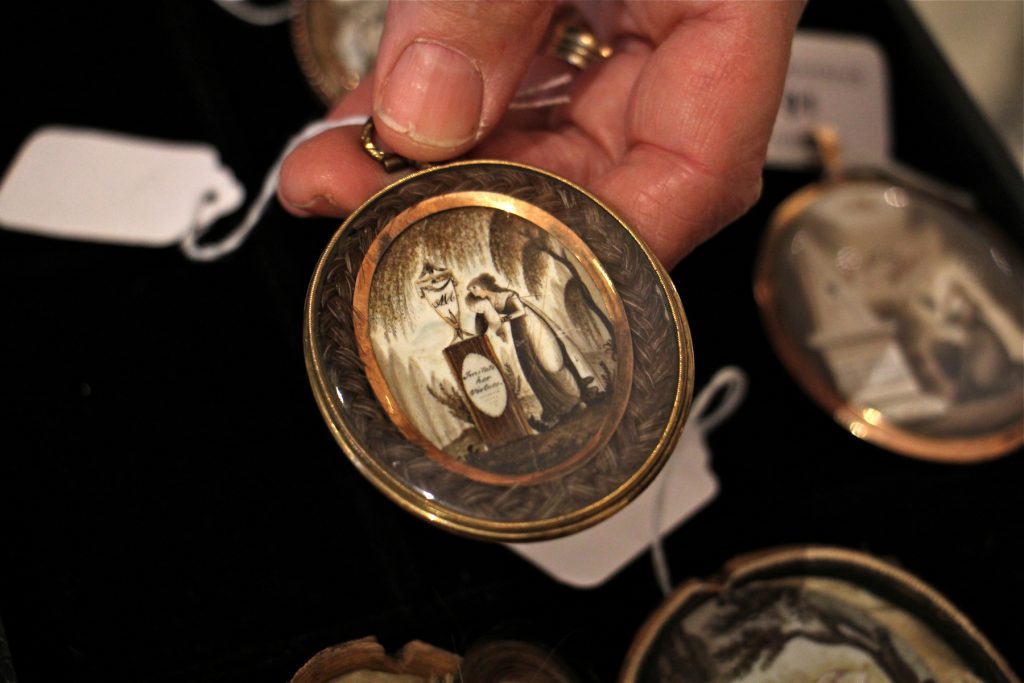 2017 11 10-e lee-philadelphia freemans auction house-mourning art-1200×800 A palm-sized oval pendant holds a painting on ivory of a woman grieving beside a gravestone. The image is framed by braided human hair.