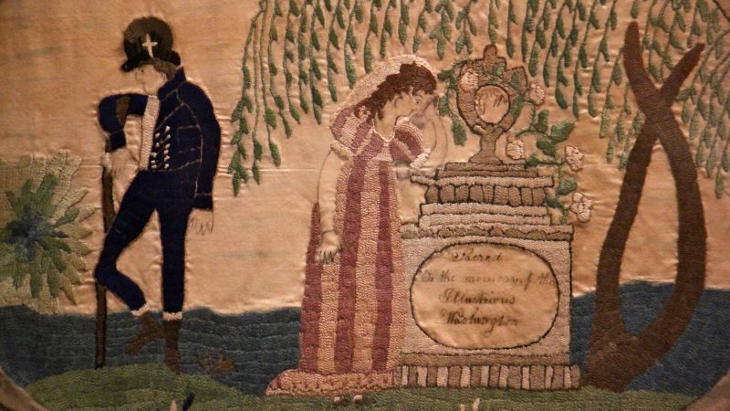 A 19th century embroidered cloth shows a woman grieving at the grave of George Washington.