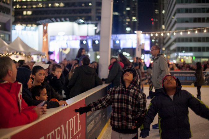 Young ice skaters look up at City Hall while gliding around the Dilworth Park skating rink. (Brad Larrison for WHYY)