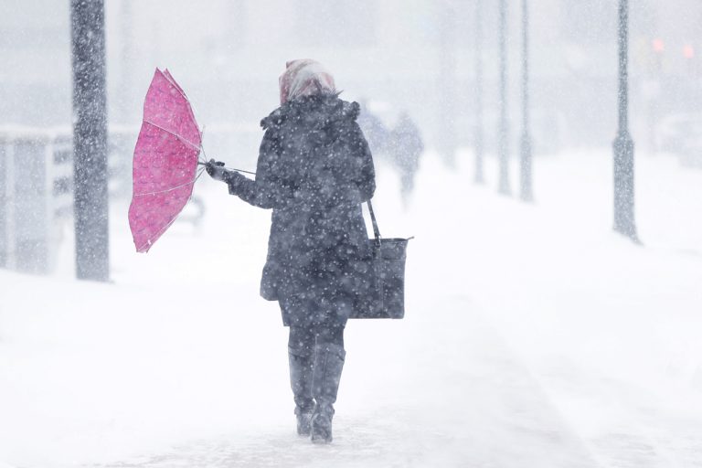 A pedestrian's umbrellas is upset during a winter snowstorm