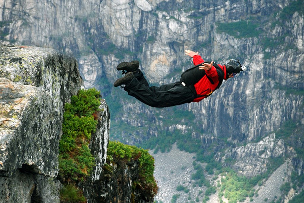 Base jump Man jumping off a cliff with a parachute