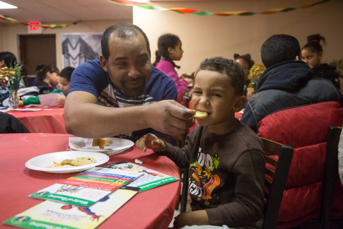 Nelson D'Jesus playfully feeds his son, Mikeli,4, a sweet at APM's Three Kings Day/Octavious celebration for diplaced families from Puerto Rico in North Philadelphia on January 12 2018. (Emily Cohen for WHYY)