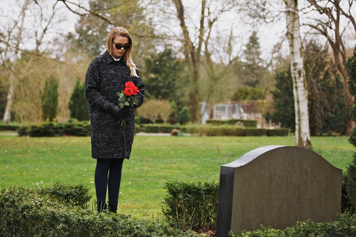 Sad Woman Grieves In A Cemetery Holding Roses Young woman visiting a loved one at the cemetery paying respects with fresh rose flowers. Female grieving at graveyard.