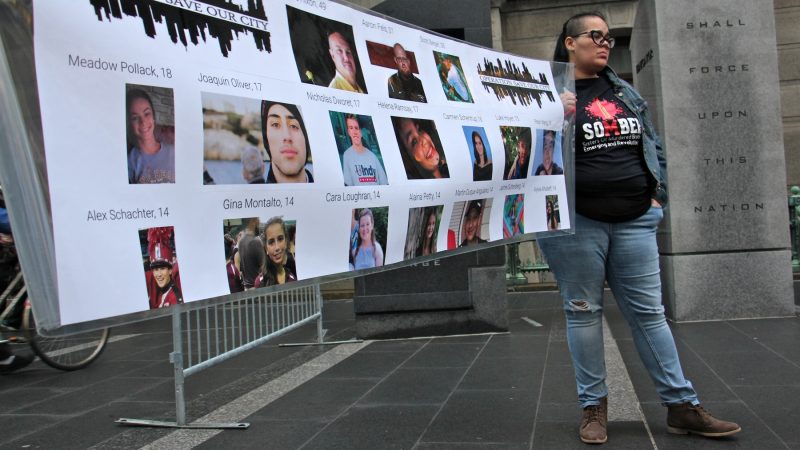Carmen Pagan of SOMBER (Sisters of Murdered Brothers Emerging and Revolutionizing), whose brother, Richard Davila was murdered two years ago, helps to hold a banner identifying the 17 people killed in the Parkland, Florida, school shooting. (Emma Lee/WHYY)