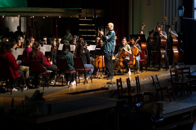 In Eagles green, Orchestra Director Ben Blazer conducts the Fly Eagles Fly song, performed by students of Central High School, during an exchange program visit of Cleveland Heights High School, the alma mater of Philadelphia Eagles center Jason Kelce. (Bastiaan Slabbers/for WHYY)