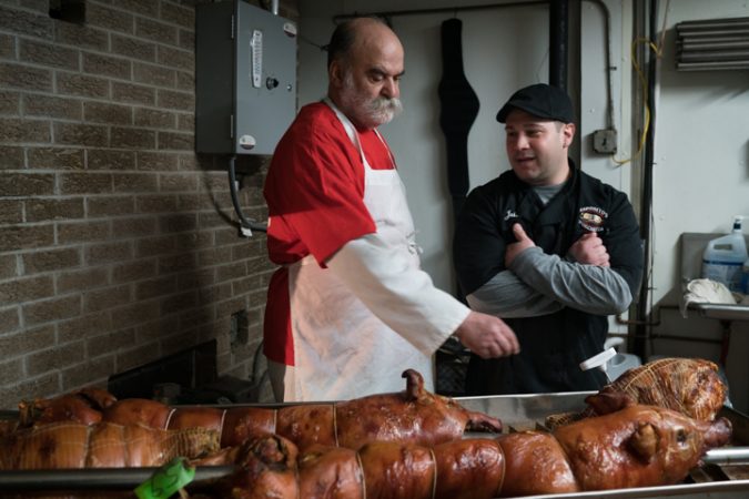 Sid Dk and Jules Esposito keep an eye on the freshly cooked pork at Esposito’s Porchetta in South Philadelphia before the Super Bowl on January 4, 2018. (Branden Eastwood for WHYY)