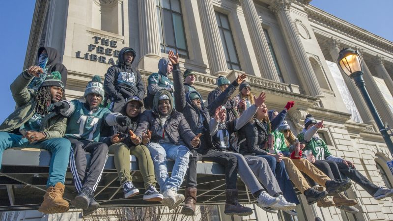 Fans cheer from atop a SEPTA bus shelter. (Jonathan Wilson for WHYY)
