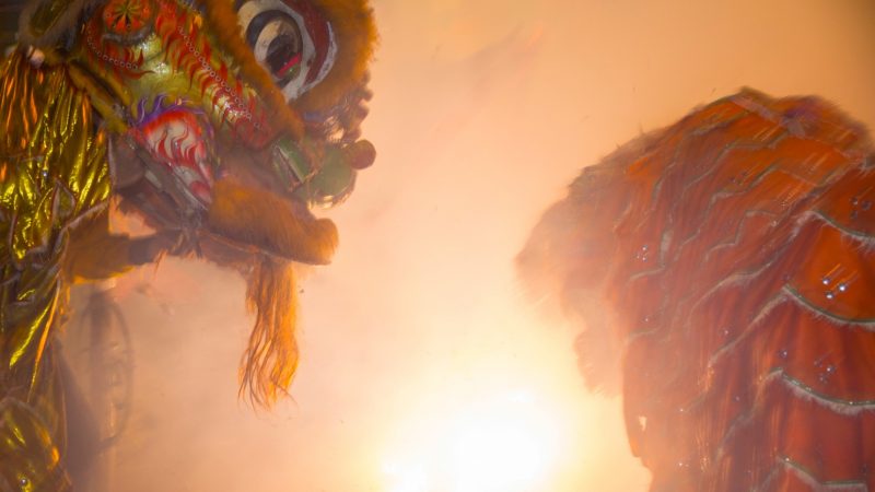 Members of the Philly Suns do a lion dance around a two-story string of firecrackers as they go off in celebration of the Chinese New Year in Phildelphia's Chinatown on February 15, 2018. (Emily Cohen for WHYY)