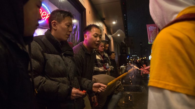 Older members of the community help the younger ones light their firecrackers during the downpour of rain that accompanied their celebration of the Chinese New Year in Phildelphia's Chinatown on February 15, 2018. (Emily Cohen for WHYY)