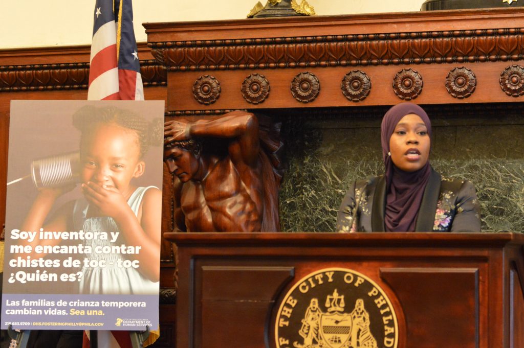 foster Stephanie Laws talks about the joys of being a foster parent, flanked by a sign with information about a new campaign to recruit more of them. (Tom MacDonald/WHYY)