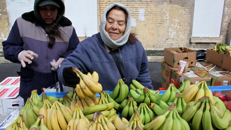 Philabundance volunteer Miriam Menard arranges bananas on a table for the free farmers market at Lillian Marrero Library. (Emma Lee/WHYY)