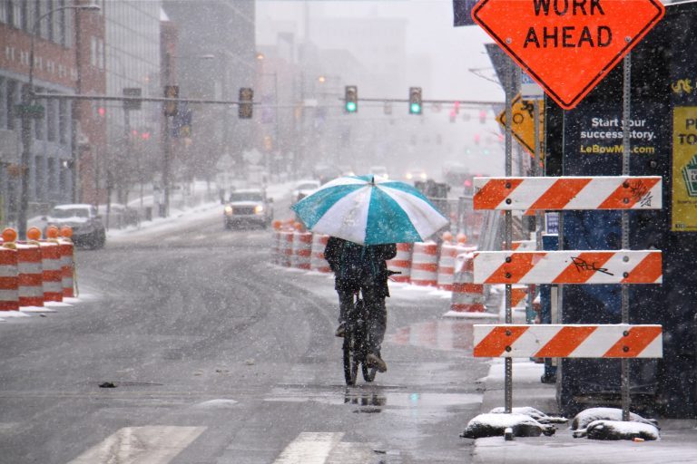 A bicyclist makes his way west on Market Street, protected from the heavy wet snow by an oversized umbrella. (Emma Lee/WHYY)