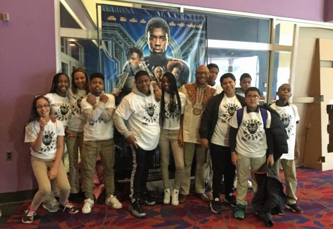 Seventh-grade English teacher, Herman Douglas, and his students pose in front of the Black Panther movie poster after seeing the movie. (Kyrie Greenberg/for WHYY)