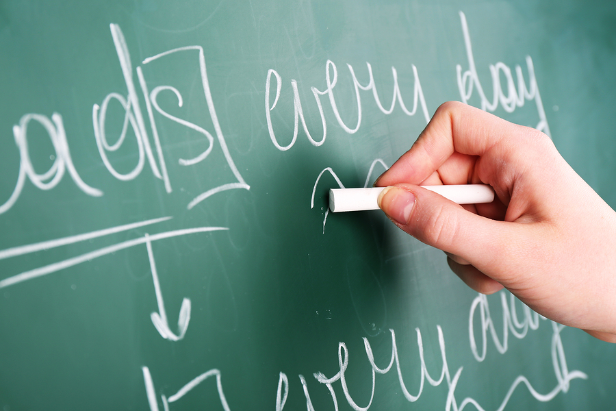 Teacher hand writing grammar sentences on blackboard background Teacher hand writing grammar sentences on blackboard background