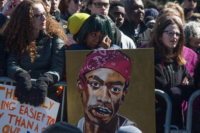 Shakira Fagan, of North Philadelphia, wipes away a tear as she holds onto a painting of her son Irell Williams who was 17 when he was shot and killed. (Emily Cohen for WHYY)