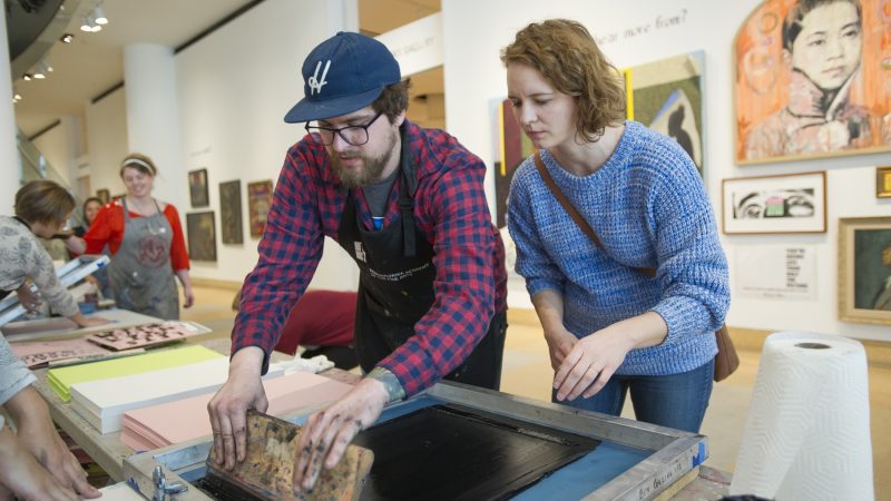 Ben Grzenia shows Kristina Murray how to squeegee a silk screen print. (Jonathan Wilson for WHYY)