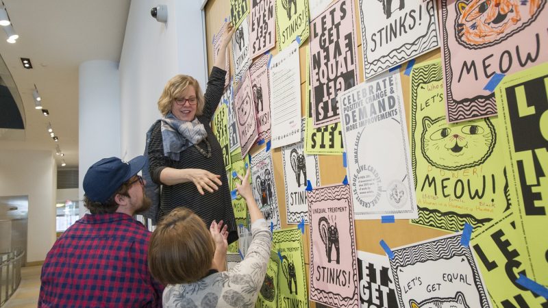 Museum Director Brooke Davis Anderson tapes protest posters to the closed doors of the Chuck Close Exhibit. (Jonathan Wilson for WHYY)