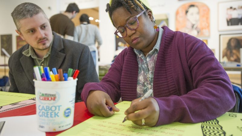 William Smith watches Marie Bjerre write a personal message on a poster. (Jonathan Wilson for WHYY)