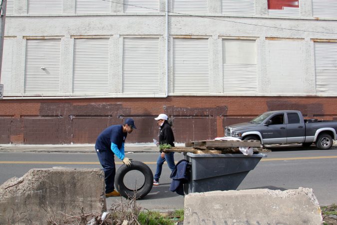Workers and volunteers pick up trash along Gurney Street near the former heroin encampment. The Jerusalem furniture warehouse across the street is being considered for a mural, part of a strategy of using art to reclaim the space. (Emma Lee/WHYY)