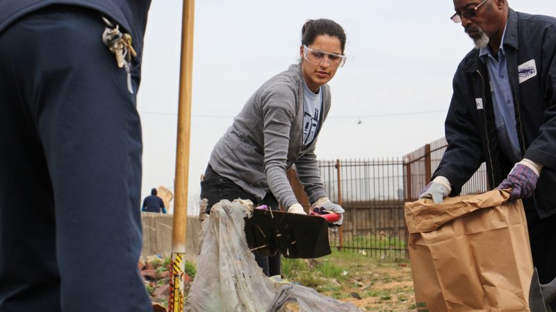 Stasia Monteiro of HACE shovels garbage into a bag during the Gurney Street cleanup. (Emma Lee/WHYY)